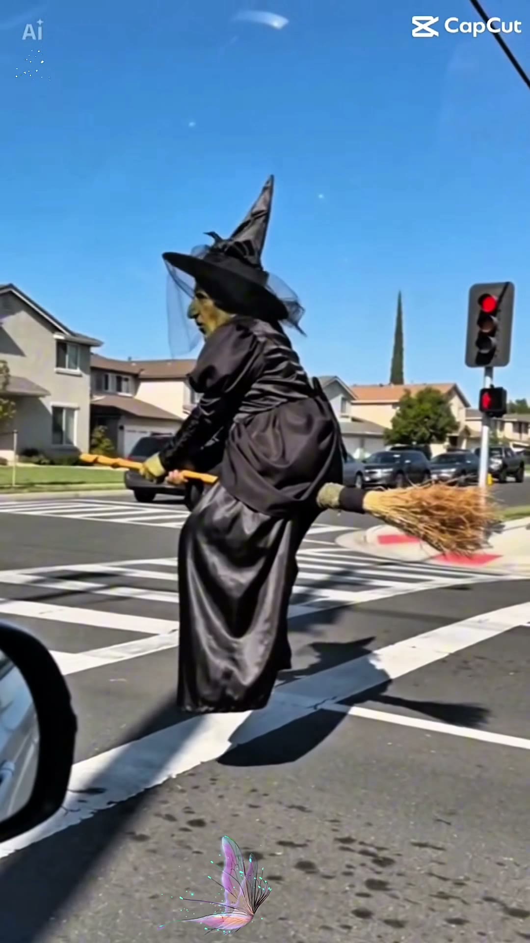 Frame from a viral broom riding video: a witch in a black dress and pointed hat flying a broom beside a car at a suburban crosswalk