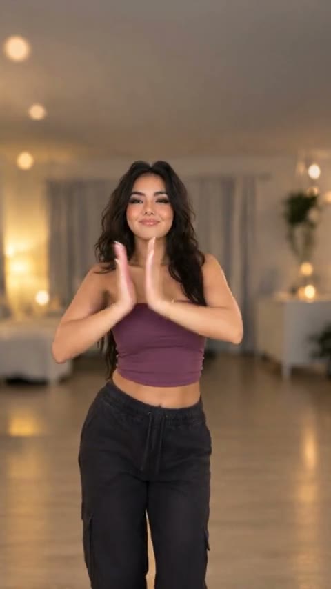 A frame from a Nicole Kidman dance TikTok: a woman in a purple top and black cargo pants with her palms pressed together in a living room