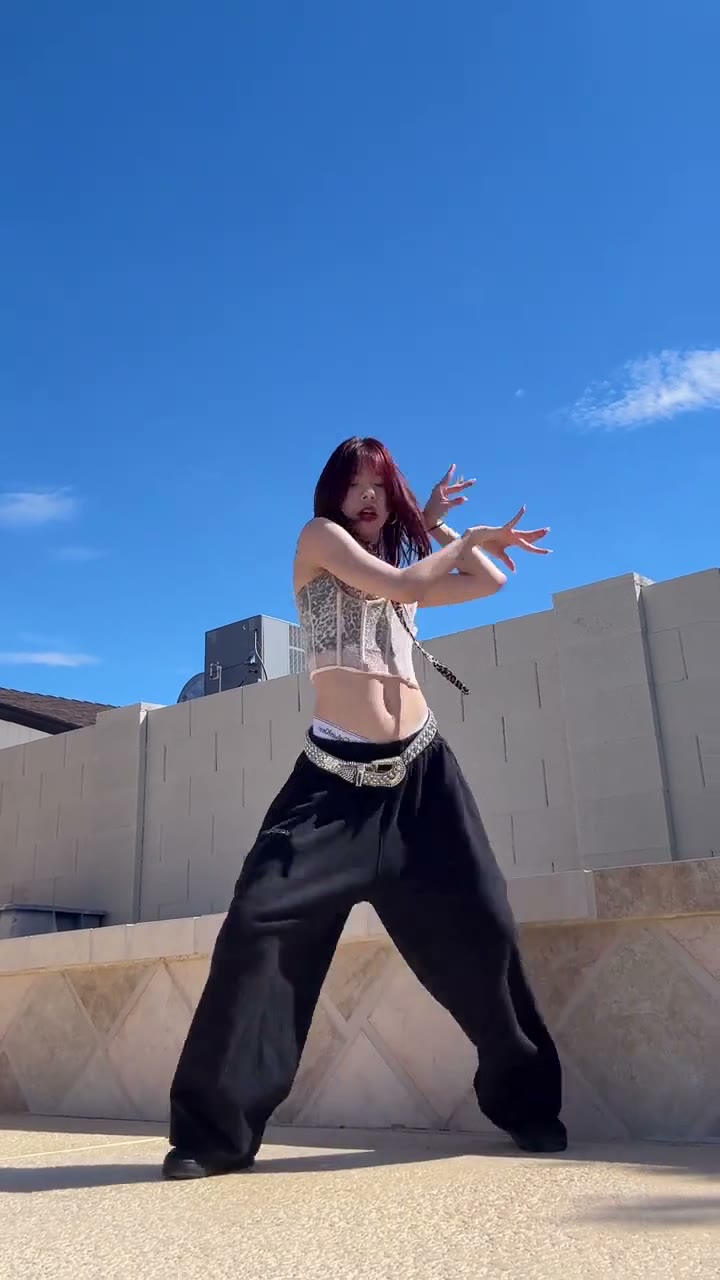A frame from the source clip: a dancer in a white top and black wide-leg trousers dancing outdoors in front of a wall and blue sky