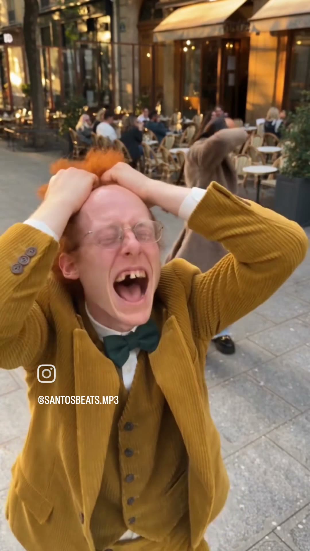 Frame from the Smalltown Boy dance clip: a dancer in a yellow corduroy suit grabbing his head, a second dancer in a brown fluffy coat behind him, café terrace in the background