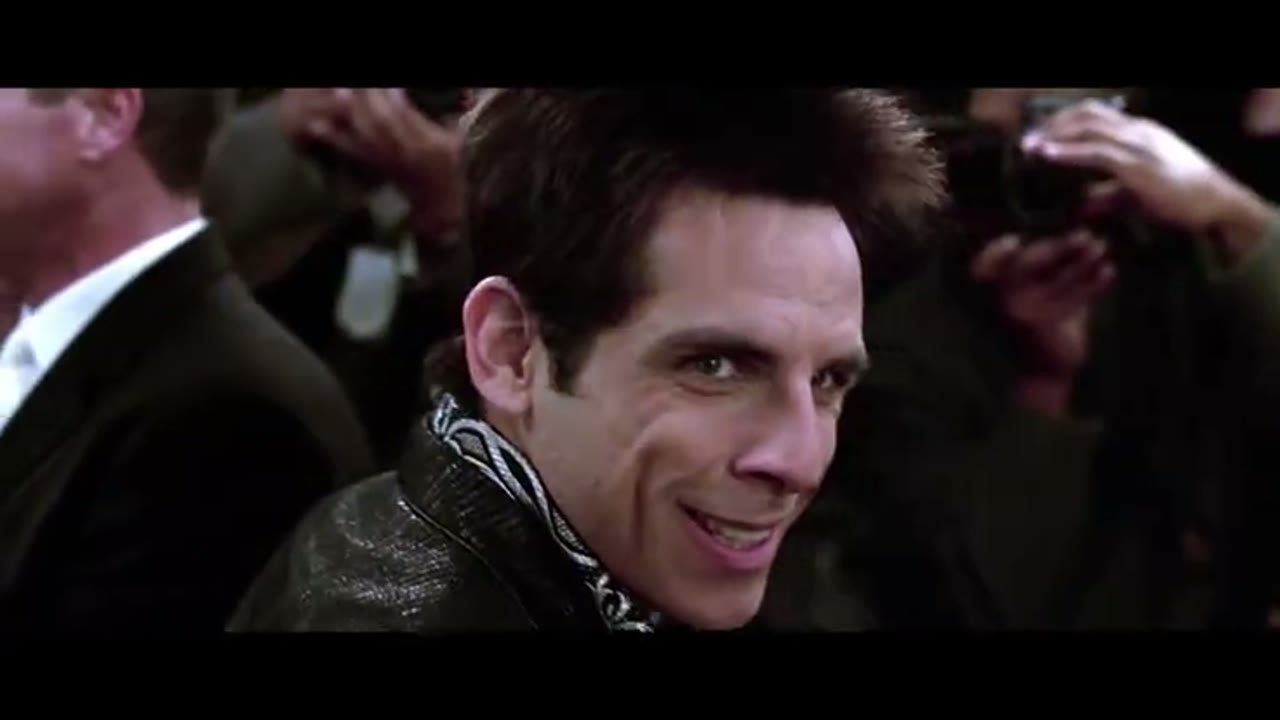 Frame from the Zoolander red-carpet scene: a model in a black jacket turning to stare, photographers in the background